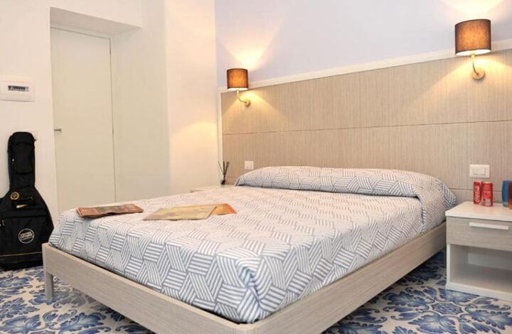 A modern bedroom featuring a queen-size bed with geometric patterned bedding, ambient wall lighting, and contemporary furnishings.