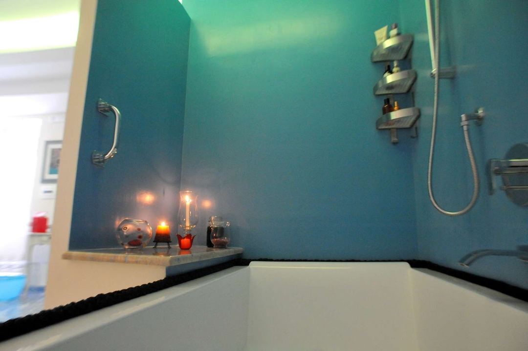 A bathroom bathtub area with turquoise walls, decorative candles and bath accessories on a shelf, and chrome shower fixtures.